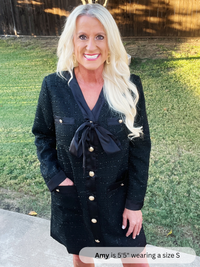 Woman wearing a black dress with gold buttons outdoors on a grassy area.