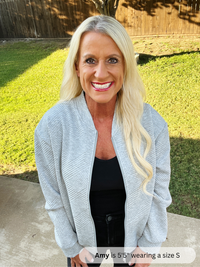 Woman wearing a gray cardigan over a black top outdoors on a sunny day.