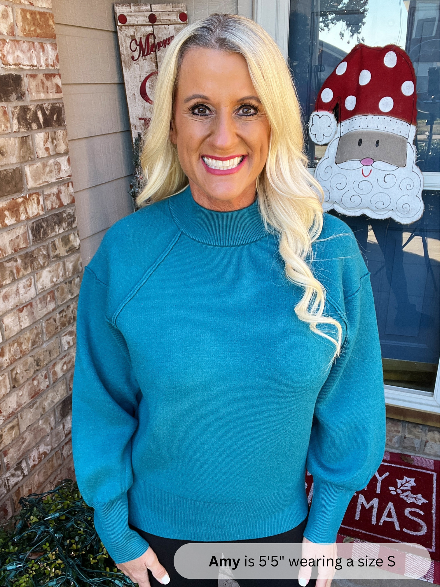 Woman wearing a blue sweater standing in front of a decorated door with a gnome and Christmas decorations.