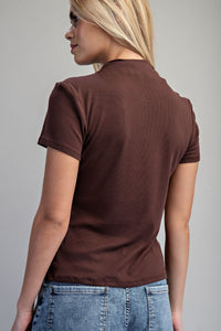 A woman wearing a brown ribbed short-sleeve t-shirt paired with light blue denim, shown from the back to display the garment's fit and texture.