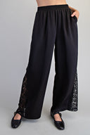 Black wide-leg pants with an elastic waistband and lace panel detailing along the lower legs. The pants feature functional side pockets and a relaxed, flowing silhouette.