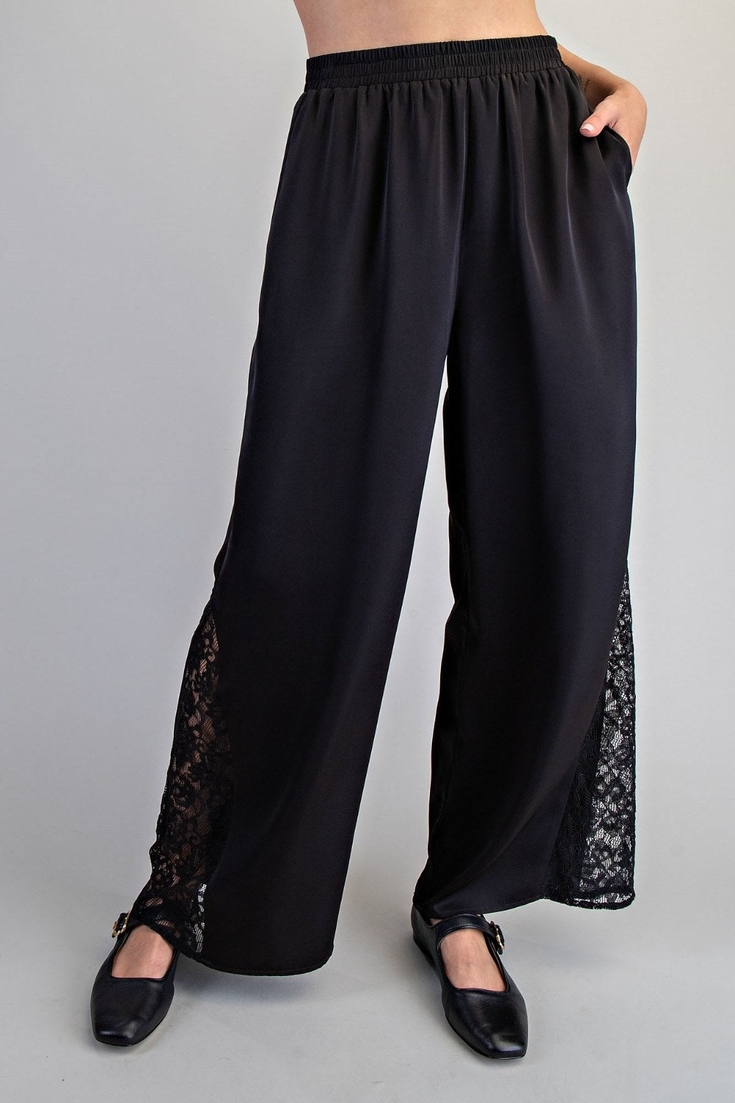 Black wide-leg pants with an elastic waistband and lace panel detailing along the lower legs. The pants feature functional side pockets and a relaxed, flowing silhouette.