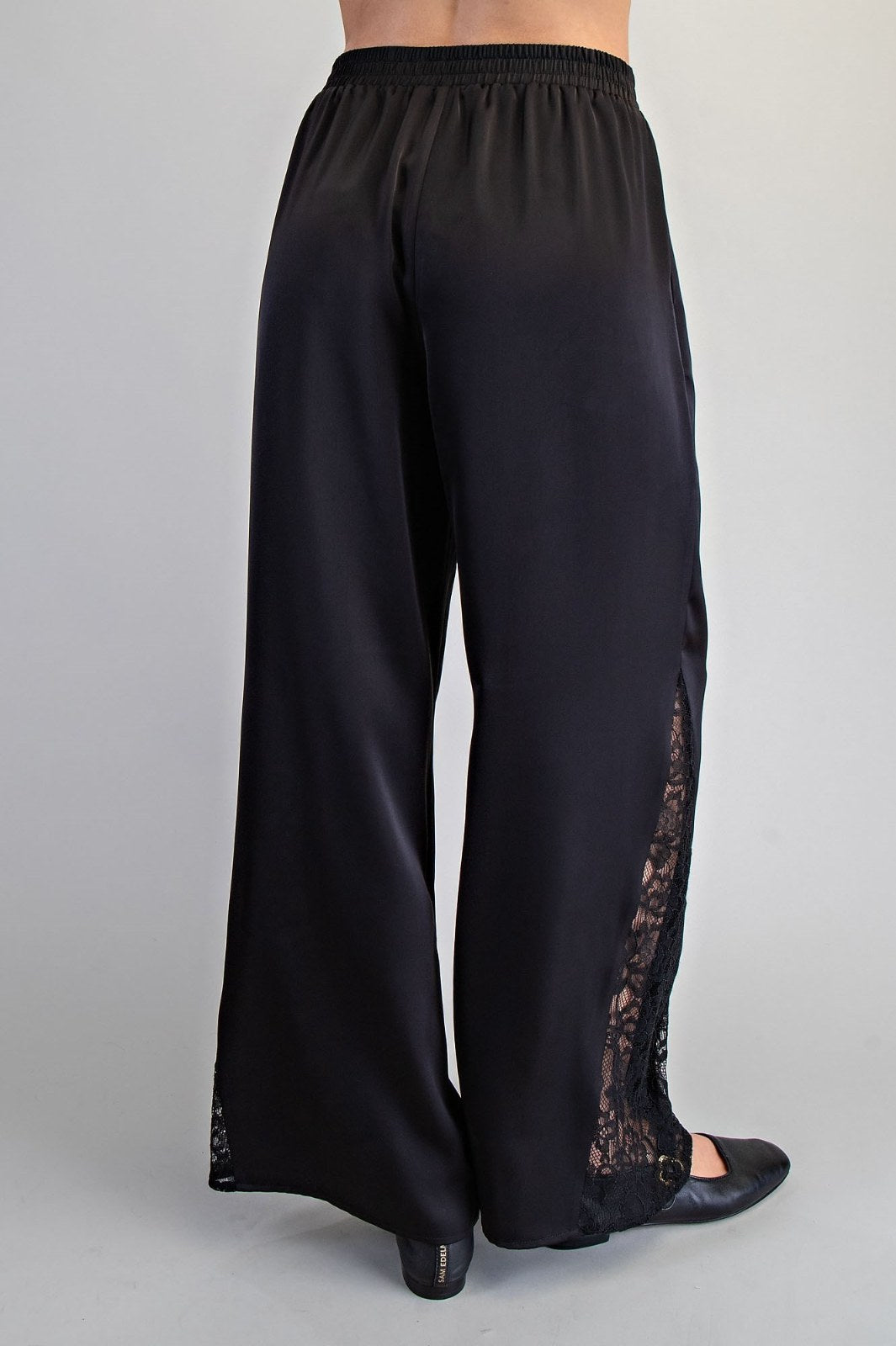 Black wide-leg pants with an elastic waistband and lace panel detailing along the outer seams, shown from the back view on a model.