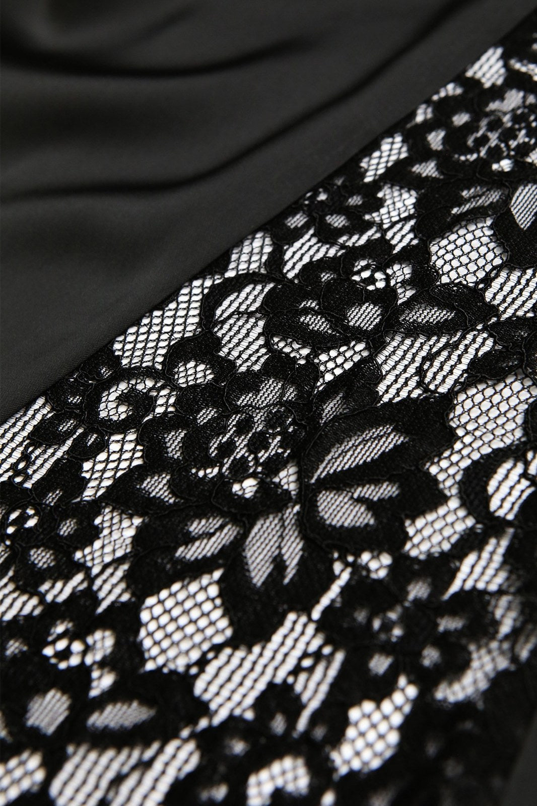 Black lace trim with an intricate floral pattern featuring open mesh details, displayed against a dark fabric background. The delicate lace showcases fine embroidered designs with a romantic, elegant aesthetic suitable for lingerie or apparel embellishment.