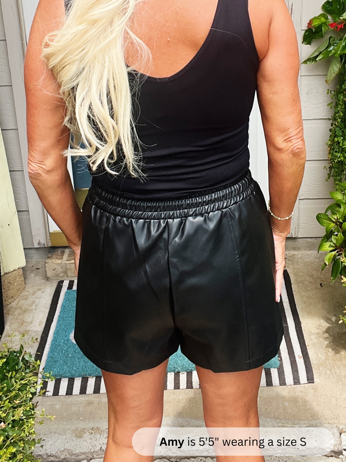 Person wearing a black tank top and black shorts standing on a porch.