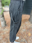 Person wearing dark gray suspenders with a blurred outdoor background