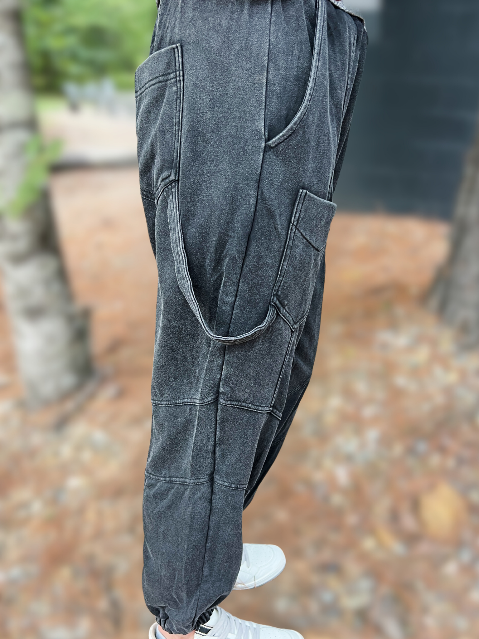 Person wearing dark gray suspenders with a blurred outdoor background