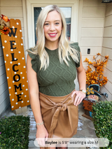 Woman standing in front of a house with 'Welcome' sign and autumn decorations