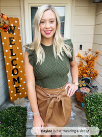 Woman standing in front of a house with 'Welcome' sign and autumn decorations