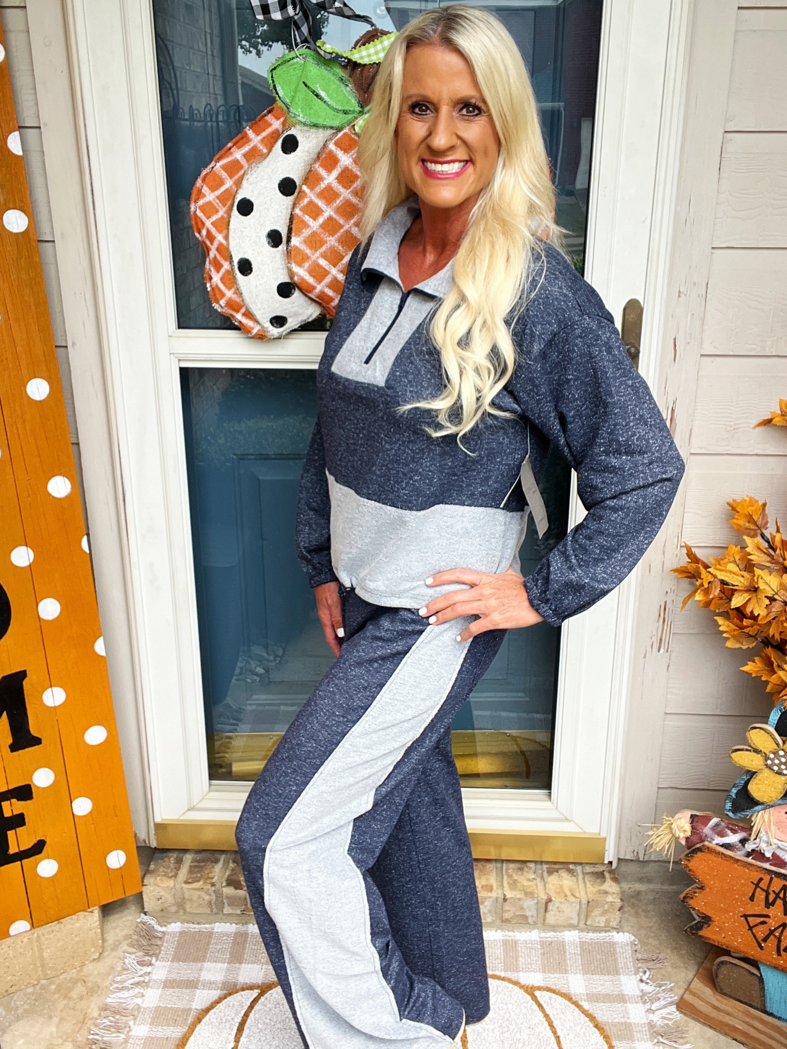 Woman in a blue and gray outfit standing in front of a decorated door with pumpkins.