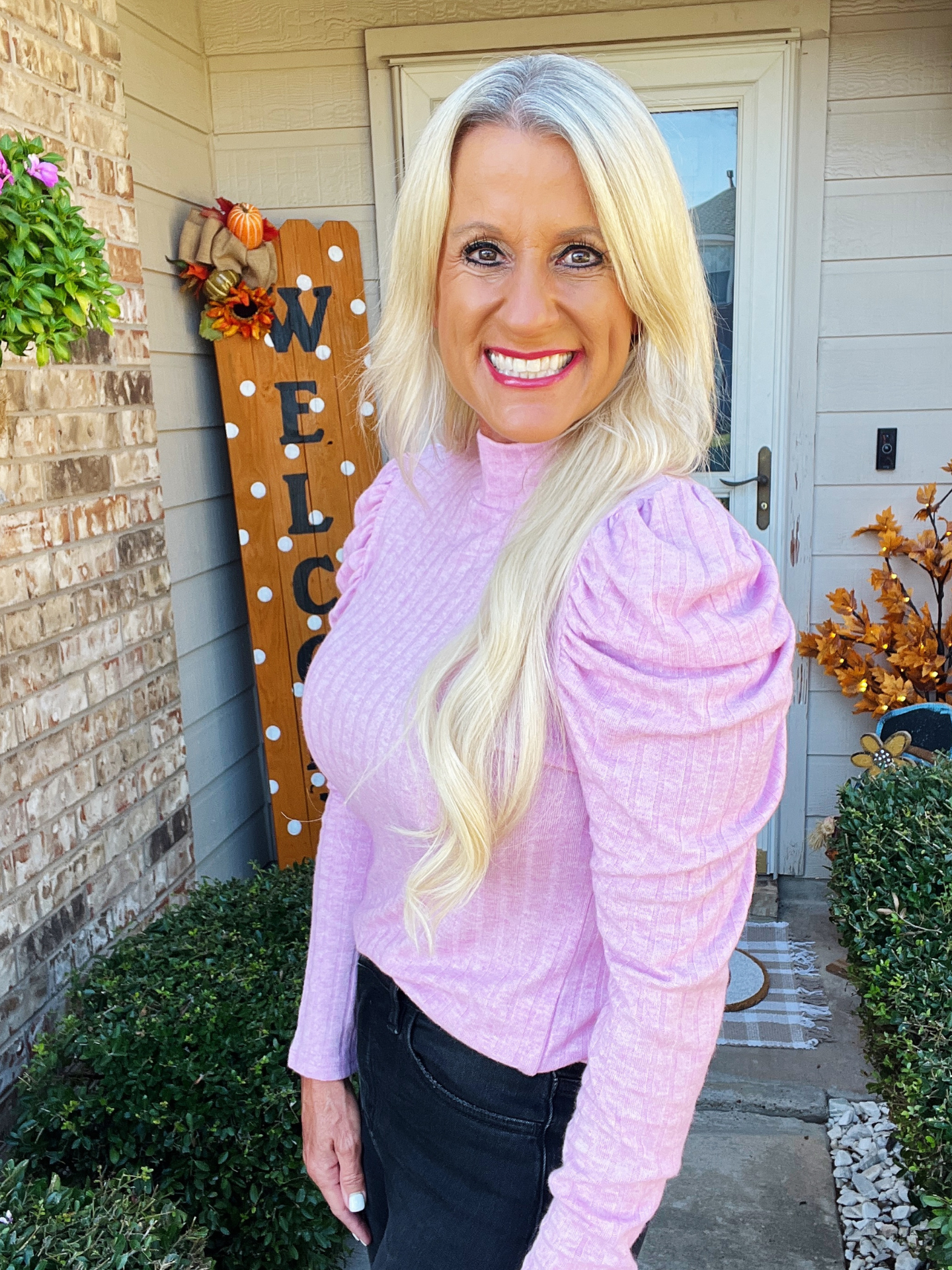 Woman in a pink sweater standing outside a house with decorative elements.