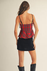 Woman wearing a red plaid camisole top with adjustable black straps and a black mini skirt, paired with black boots, shown from the back against a neutral background.