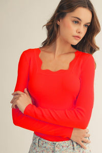 A woman wearing a bright red long-sleeve ribbed top with a sweetheart neckline and puffed shoulders, paired with a floral patterned skirt.