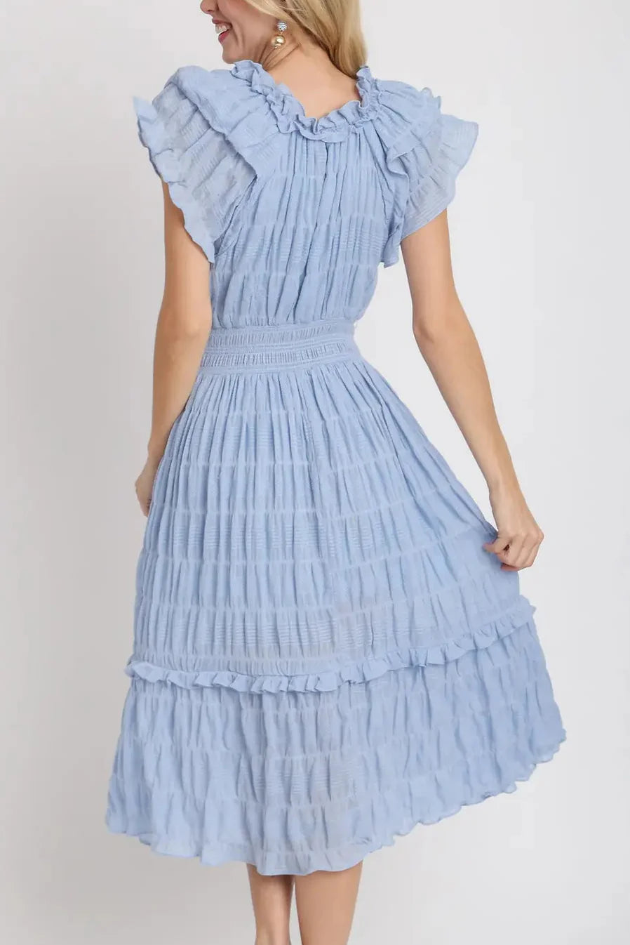 Woman wearing a light blue dress with ruffled sleeves and layers on a white background
