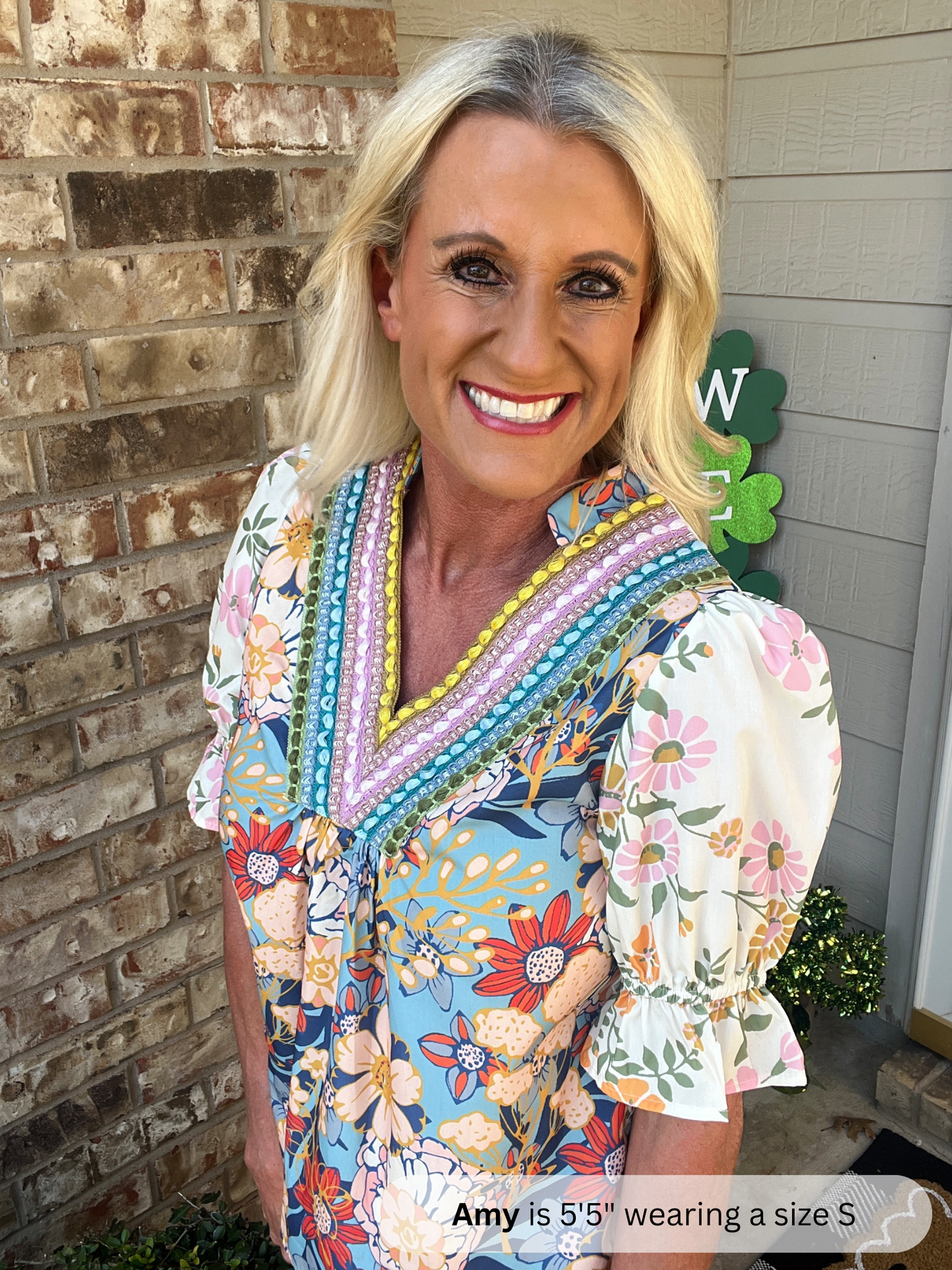 Woman wearing a colorful patterned dress standing in front of a brick wall.