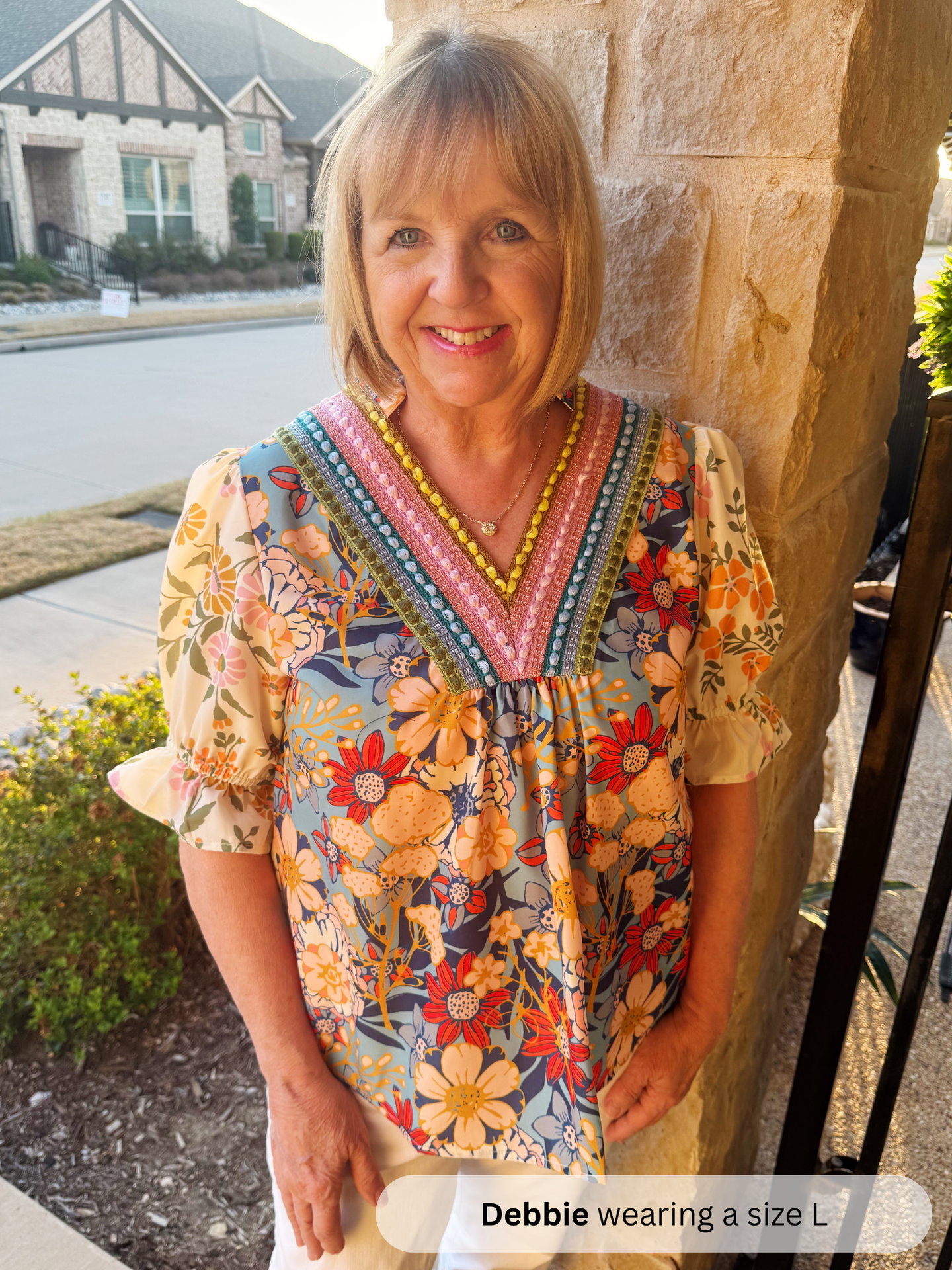 Woman wearing a colorful dress standing outdoors next to a stone wall.