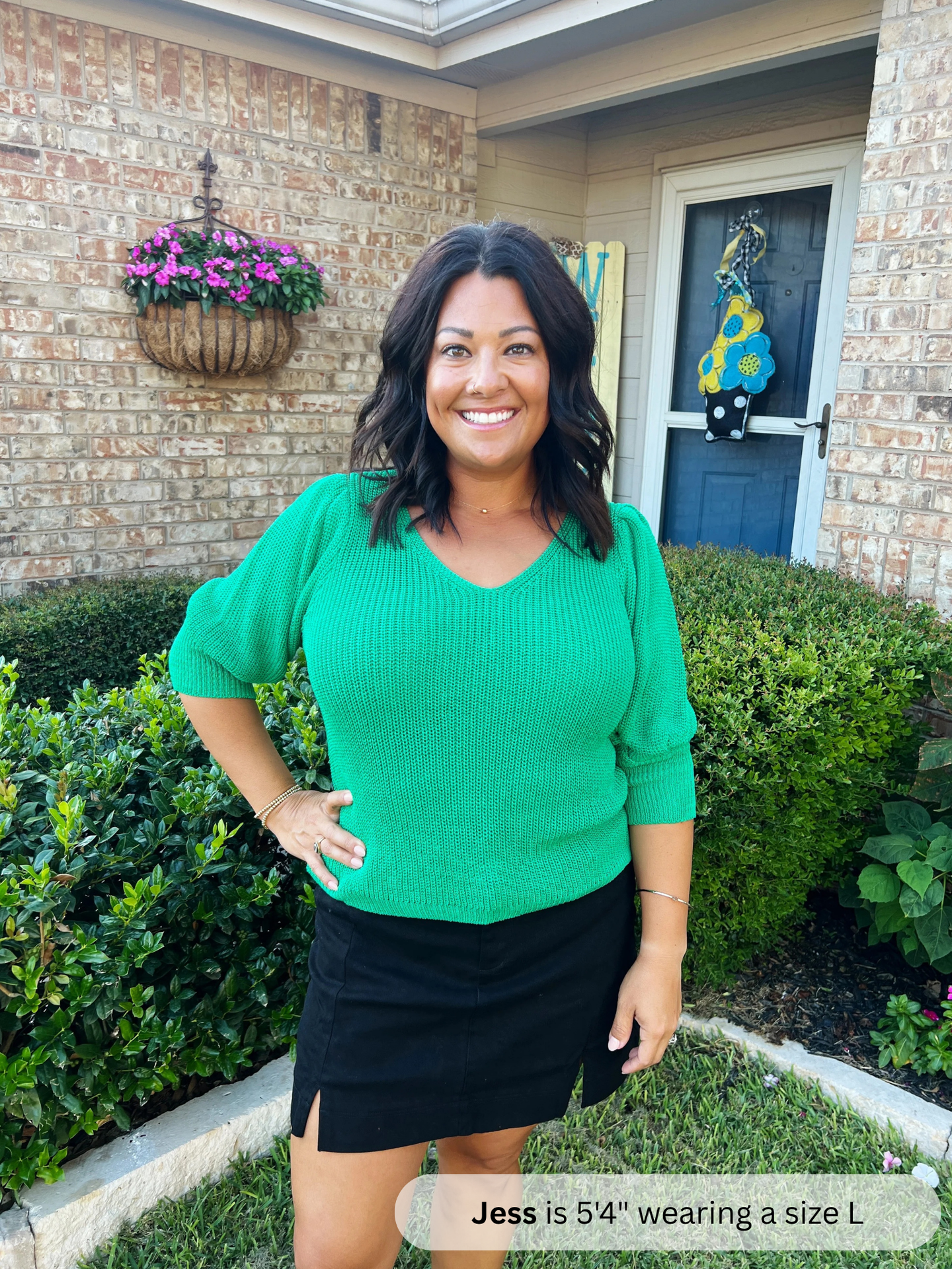 Woman in a green top and black skirt standing in front of a house with decorative elements.