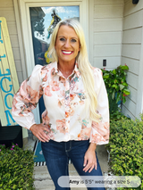 Woman wearing a floral blouse and jeans standing outside a house.