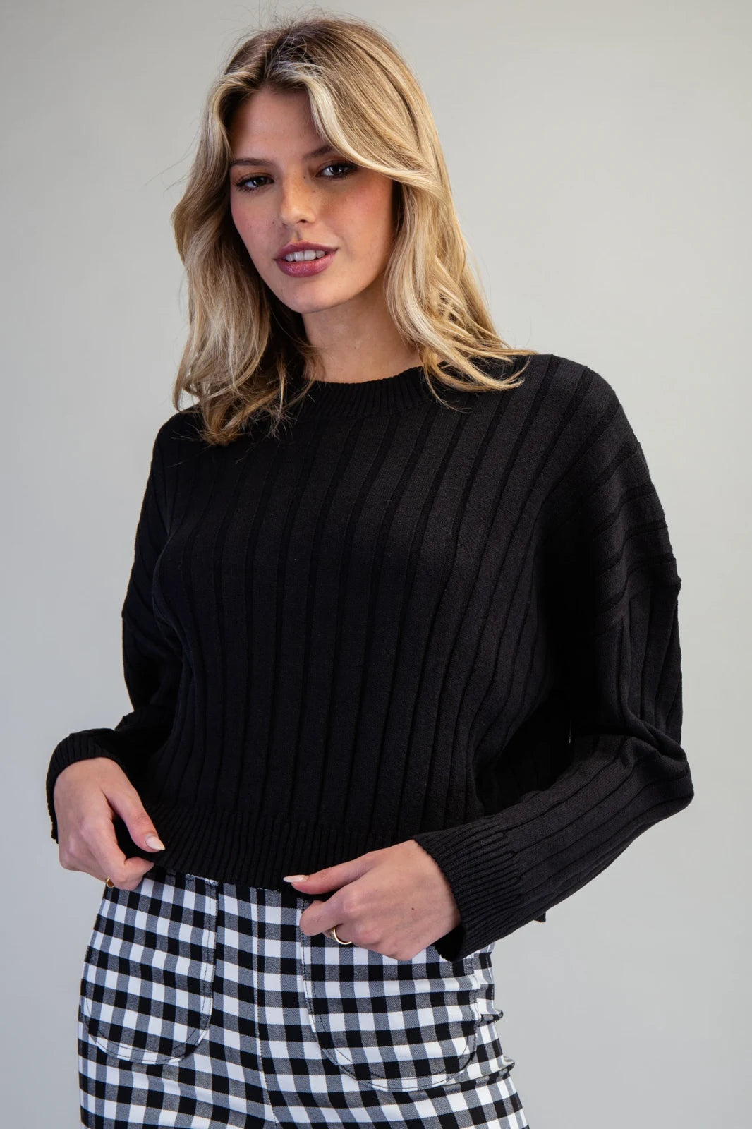 A woman wearing a black ribbed crew-neck sweater paired with a black and white gingham check skirt, styled for a classic casual look.