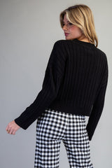 A person wearing a black ribbed knit sweater paired with black and white gingham check pants, shown from a three-quarter back view against a neutral gray background.