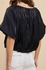 Woman wearing a black blouse with short sleeves on a beige background
