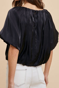Woman wearing a black blouse with short sleeves on a beige background