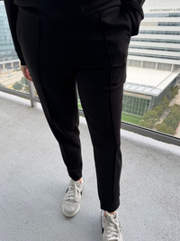 Person wearing black pants and white sneakers standing in a room with large windows.
