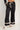 Black wide-leg lounge pants with an elastic waistband and cream drawstring, featuring decorative lace trim at the cuffs and waist. Modeled with matching black and cream fuzzy slippers.