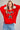 A woman wearing a bright red crew neck sweatshirt featuring a festive candy cane design with a red bow, paired with light blue jeans.