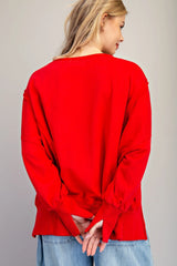 A woman wearing a bright red long-sleeve top with ruffled bell cuffs, shown from the back, paired with light blue denim jeans against a neutral background.