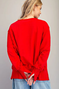 A woman wearing a bright red long-sleeve top with ruffled bell cuffs, shown from the back, paired with light blue denim jeans against a neutral background.