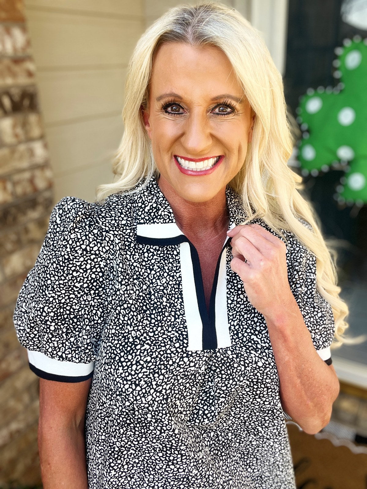 Woman wearing a short-sleeved black and white speckled blouse with white and black trim detailing around the neckline and cuffs.