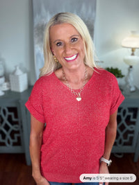Woman wearing a short-sleeved red knit sweater with a crew neckline and rolled cuffs, styled with a silver pendant necklace and jeans.