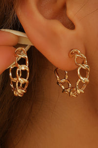 Gold chain hoop earrings worn on an ear with a blurred background
