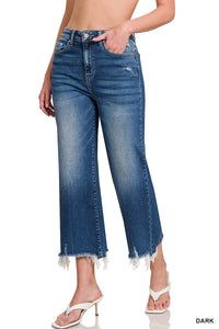 A woman wearing high-waisted, dark blue cropped jeans with a distressed frayed hem, paired with white slide sandals. The jeans feature a classic five-pocket design and sit at the natural waist with a straight-leg silhouette.