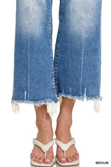 A person wearing medium-sized blue jeans with distressed, frayed raw-edge hems, paired with white thong sandals.