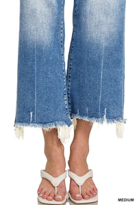 A person wearing medium-sized blue jeans with distressed, frayed raw-edge hems, paired with white thong sandals.