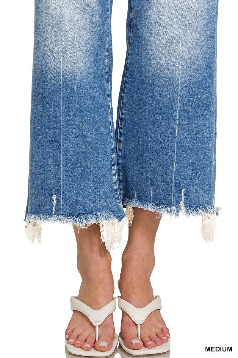 A person wearing medium-sized blue jeans with distressed, frayed raw-edge hems, paired with white thong sandals.