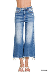 A woman wearing medium-wash blue jeans with a high waist and wide-leg crop cut, featuring distressed detailing at the thighs and frayed edges at the ankles.