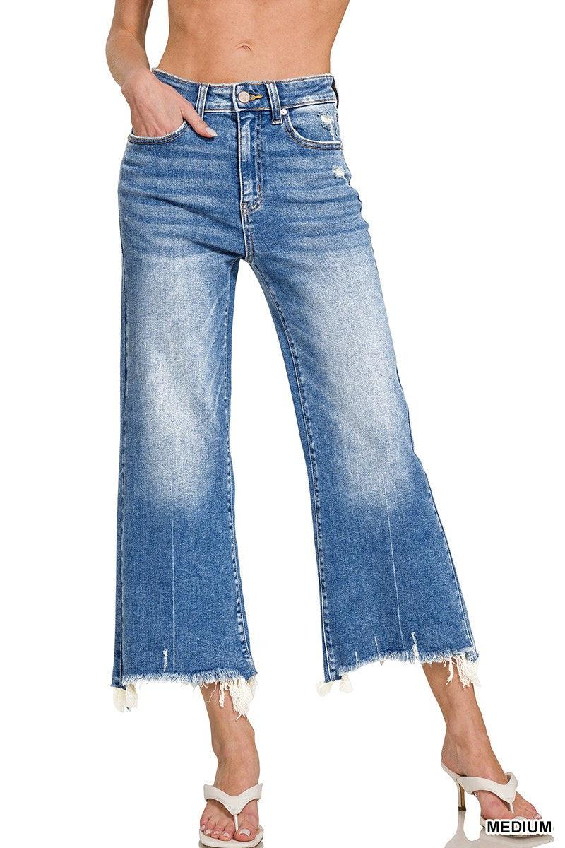 A person wearing medium-wash blue jeans with a high waist and wide-leg silhouette, featuring distressed raw hems at the cropped ankles and traditional five-pocket styling.
