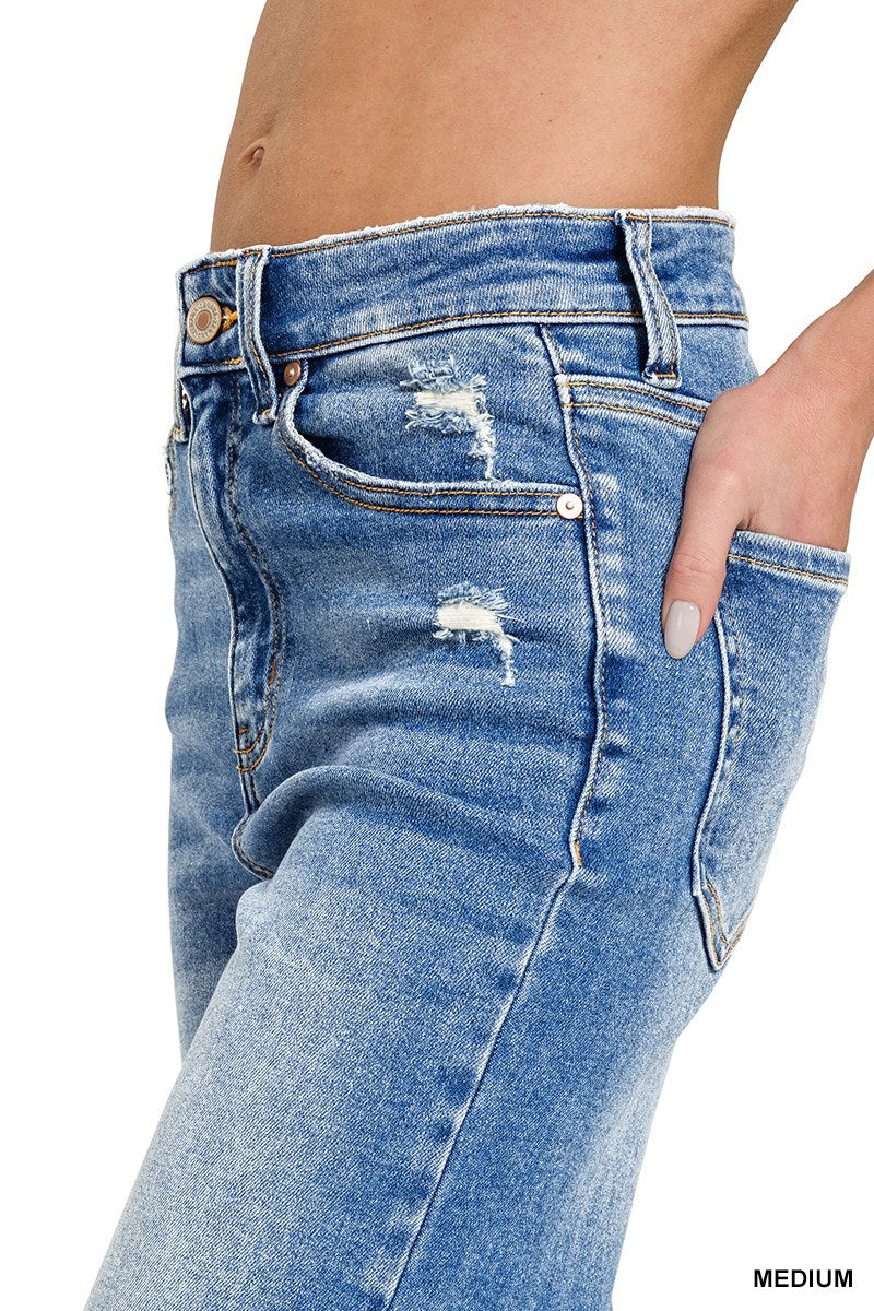 Close-up side view of medium-wash distressed blue jeans with ripped details on the thighs, featuring a classic five-pocket design and white contrast stitching.
