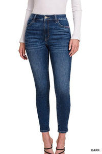 A woman wears dark blue cropped skinny jeans with a high waist and classic five-pocket styling, paired with a white ribbed long-sleeve top and black strappy heels.