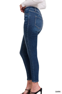 A woman wearing dark blue cropped jeans with a high waist, classic five-pocket styling, and a white ribbed long-sleeve top, shown from the side profile.
