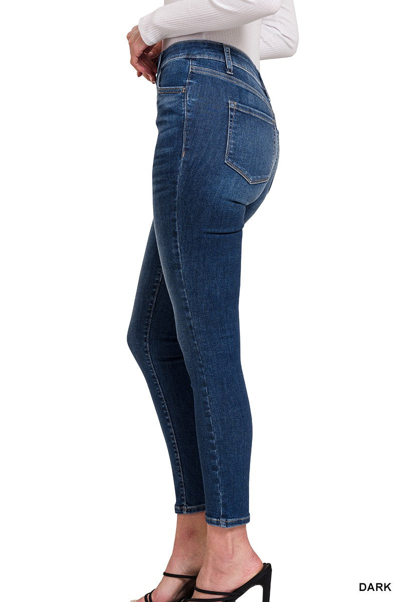 A woman wearing dark blue cropped jeans with a high waist, classic five-pocket styling, and a white ribbed long-sleeve top, shown from the side profile.
