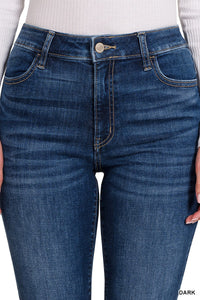 Dark blue denim jeans with a classic five-pocket design, featuring a high waistband with a button and zip closure, shown on a model wearing a white ribbed long-sleeve top.
