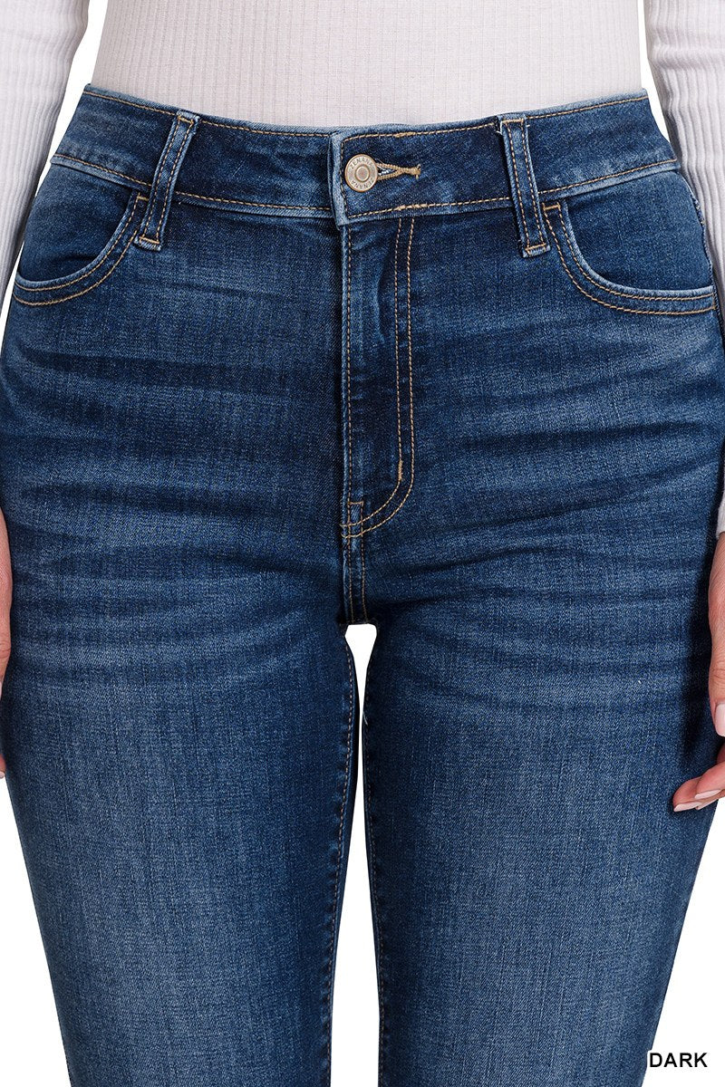 Dark blue denim jeans with a classic five-pocket design, featuring a high waistband with a button and zip closure, shown on a model wearing a white ribbed long-sleeve top.