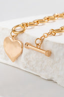 Gold-toned chain bracelet with a polished heart charm and toggle clasp, displayed on a white marble stone surface.