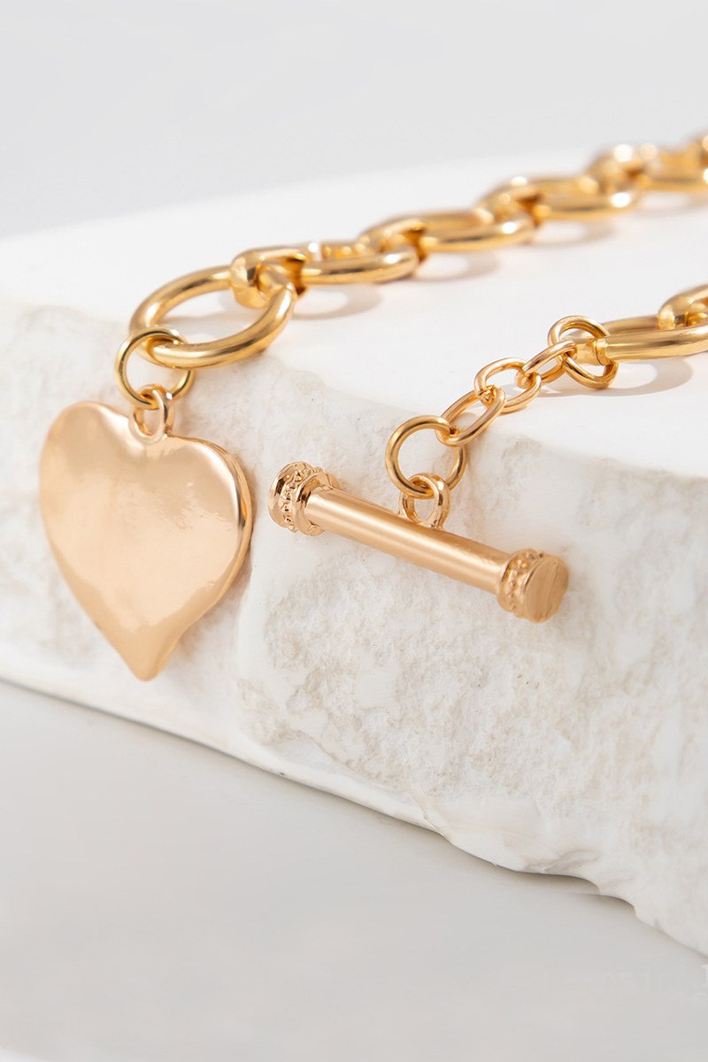 Gold-toned chain bracelet with a polished heart charm and toggle clasp, displayed on a white marble stone surface.
