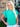 A woman wearing a turquoise ribbed knit sweater with short ruffled flutter sleeves and a crew neckline, paired with white pants.