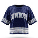 A navy blue sequined short-sleeve sweatshirt featuring "COWBOYS" in white and silver lettered appliqué across the chest, with matching silver sequined stripes on the sleeves and hem.